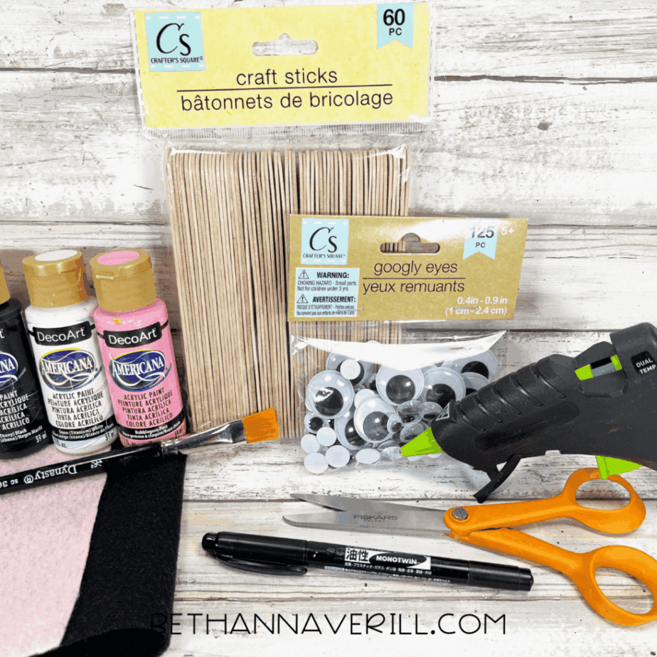 Materials for cow popsicle stick craft: paint, felt, googly eyes, scissors, glue gun, and craft sticks.