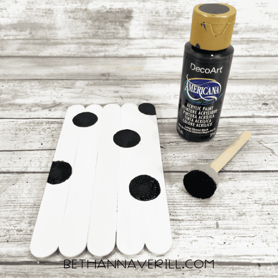 Black spots painted onto white popsicle sticks for cow pattern.
