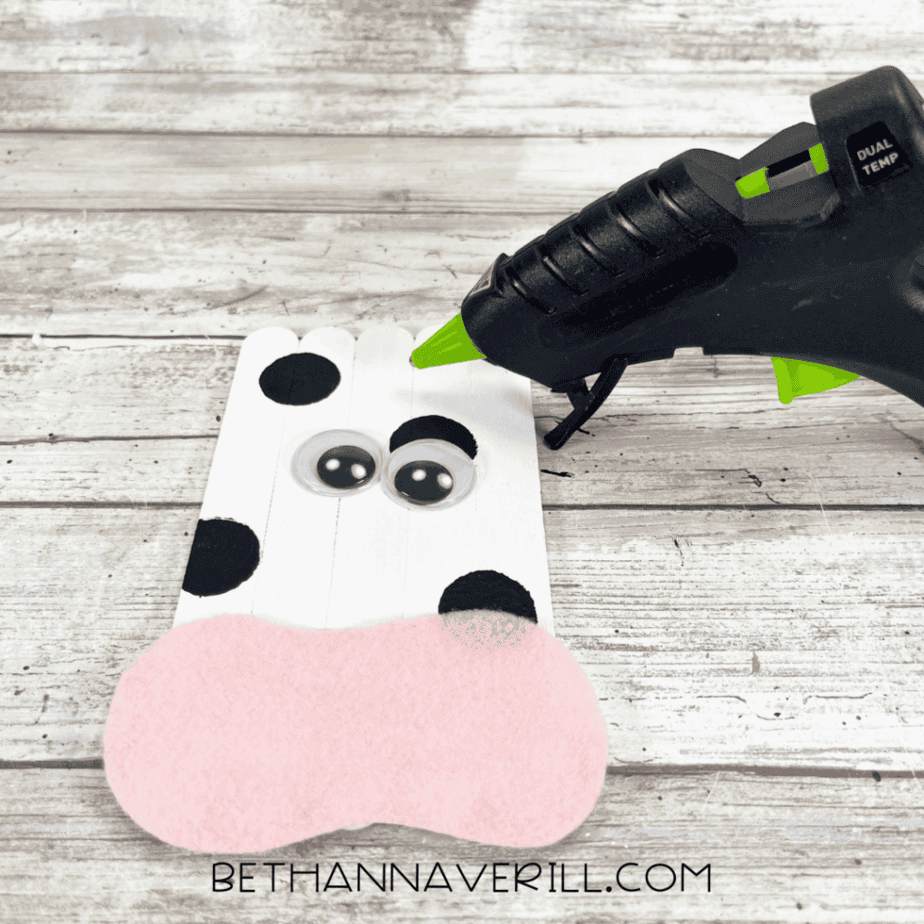 Googly eyes and pink felt snout glued onto popsicle stick cow face.