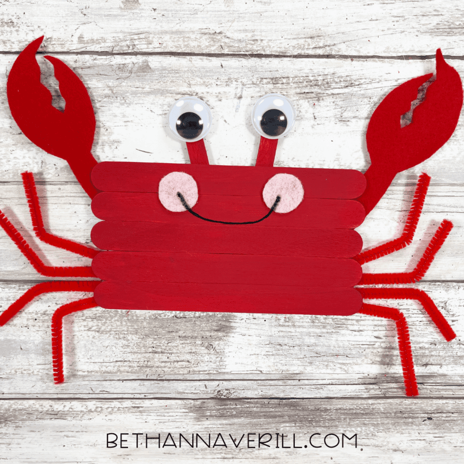 Completed crab popsicle stick craft with googly eyes, claws, and legs.