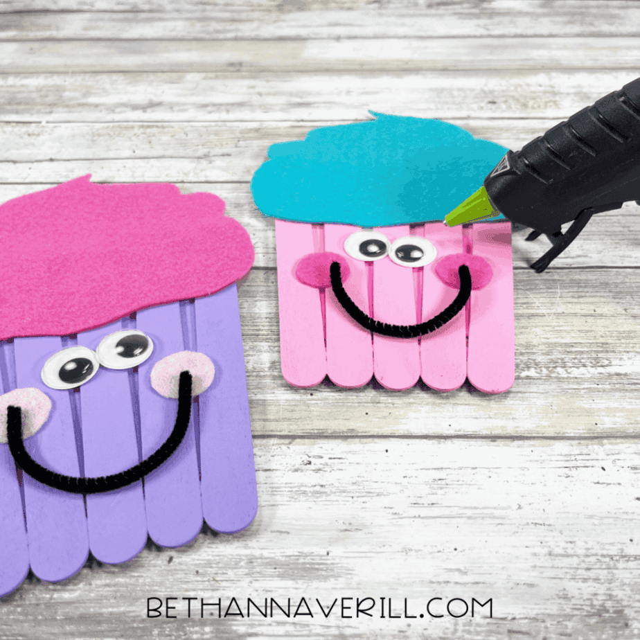 Two finished cupcake crafts with googly eyes, felt cheeks, and smiling mouths made of pipe cleaners, being glued together.