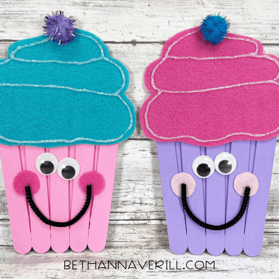 Pink and purple cupcake crafts side by side, fully decorated with googly eyes, pom-poms, felt frosting, and glittery accents.