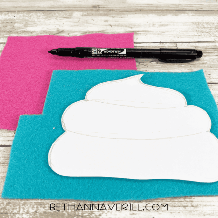 A white cupcake top template traced onto blue and pink felt sheets, with a black marker placed above them.