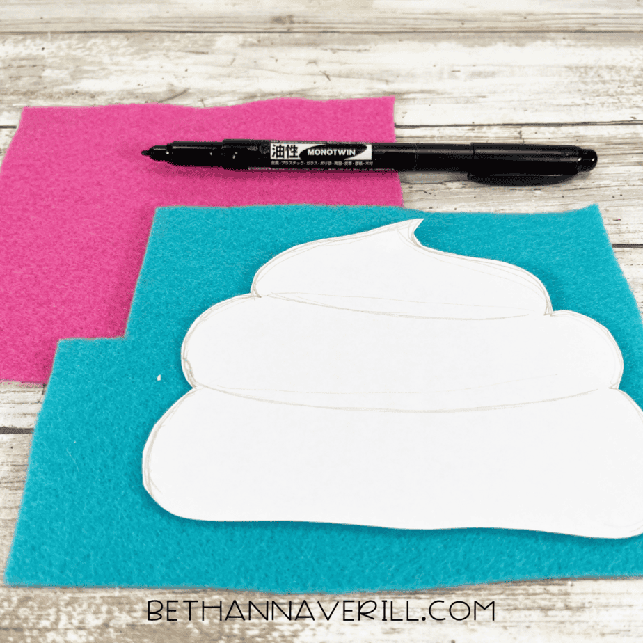 A white cupcake top template traced onto blue and pink felt sheets, with a black marker placed above them.