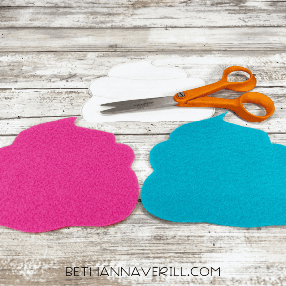 Two cupcake tops cut out of pink and blue felt, shown next to the paper template and scissors.
