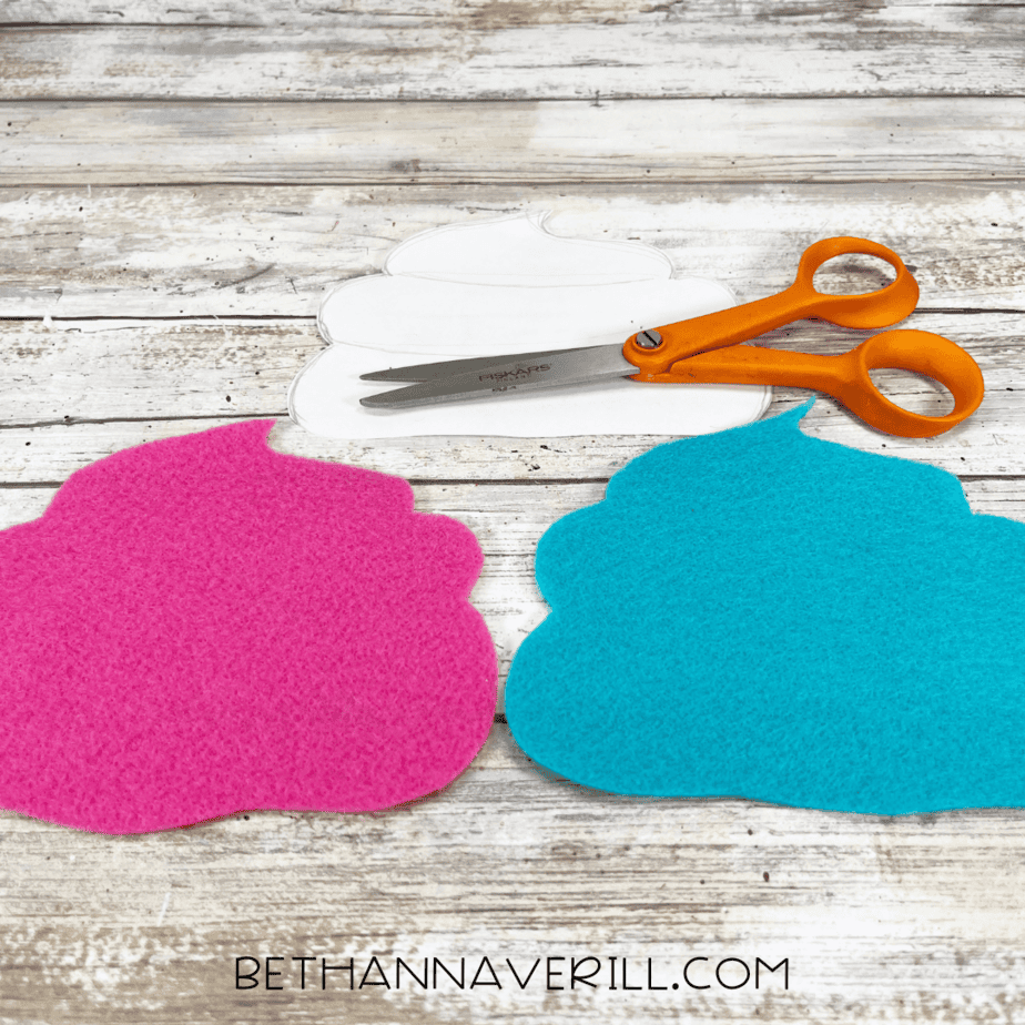 Two cupcake tops cut out of pink and blue felt, shown next to the paper template and scissors.