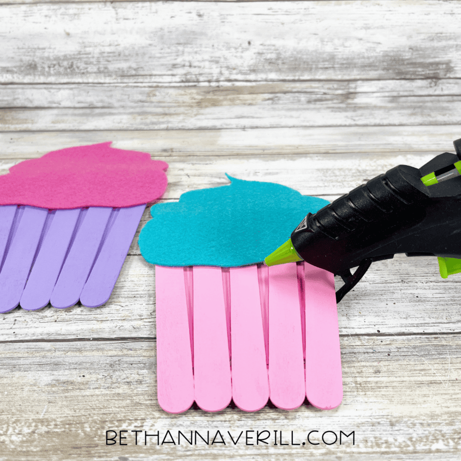 The felt cupcake tops being hot glued to the top of the painted popsicle stick panels to create the cupcake shape.