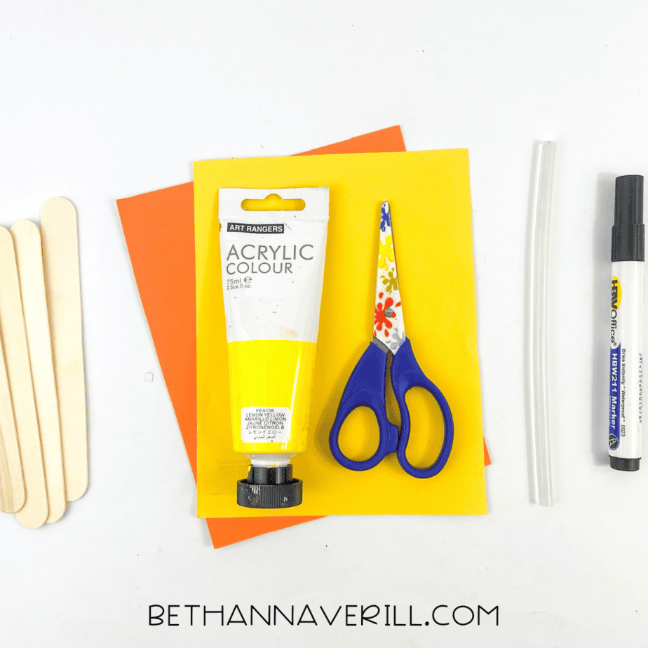 Duck popsicle stick craft supplies including popsicle sticks, yellow paint, orange and yellow paper, scissors, glue, and a marker.