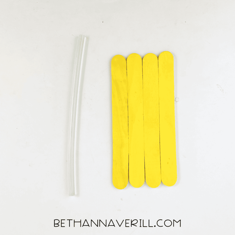 Painted yellow popsicle sticks lined up together with a glue stick beside them.