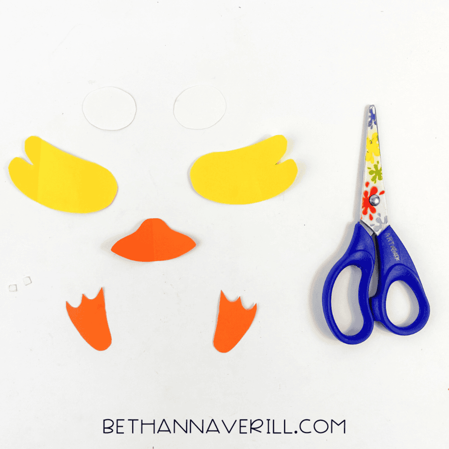Cut-out duck parts including wings, beak, feet, and eyes on white background with scissors.