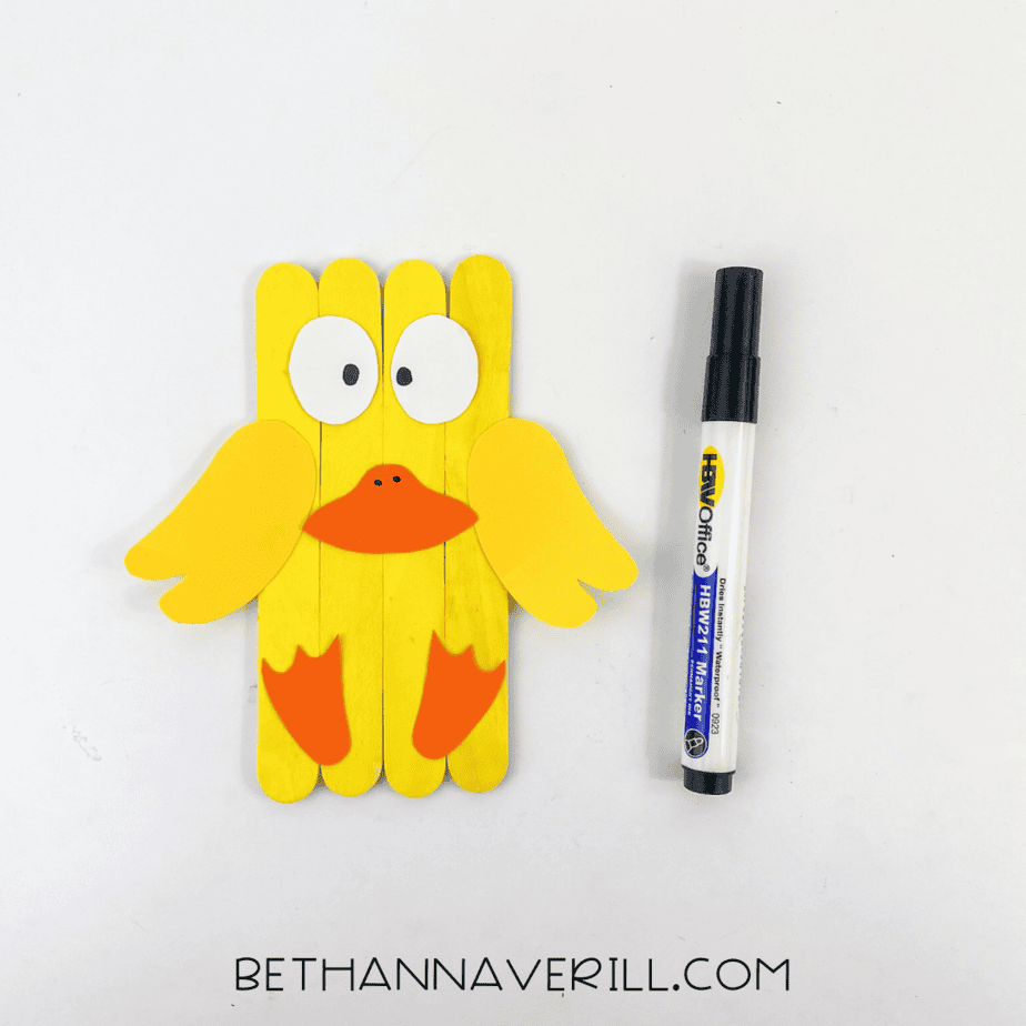 Duck popsicle stick craft with pupils and beak details drawn in with marker.