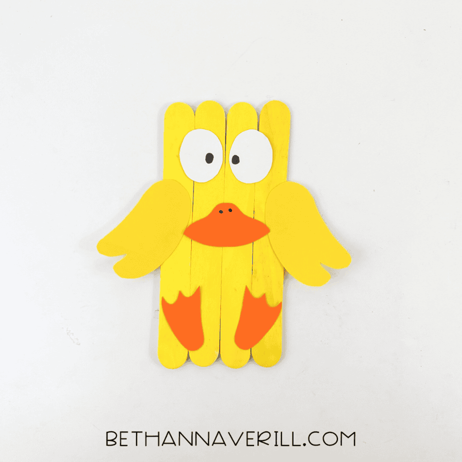 Completed duck popsicle stick craft with bright yellow body, orange beak, wings, and feet.