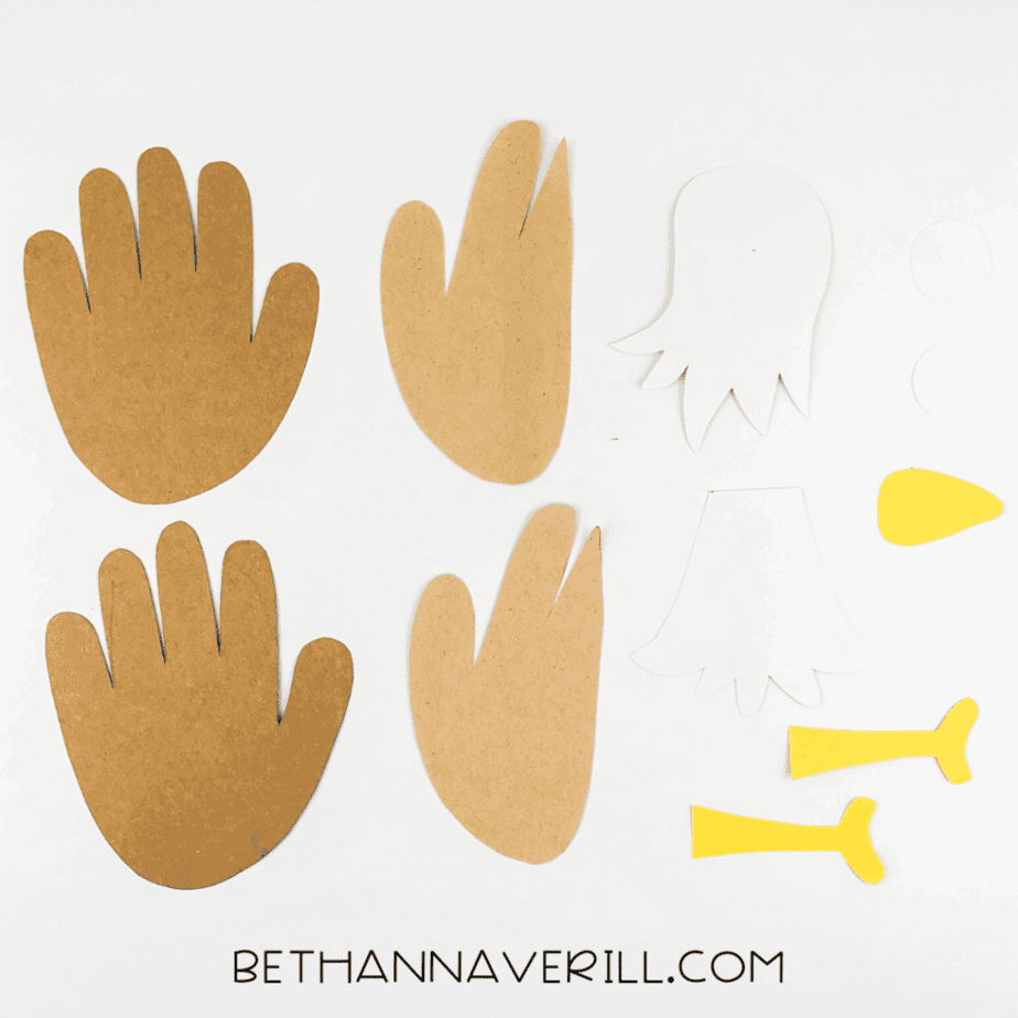 Cut-out handprints and eagle body pieces in brown, white, and yellow paper