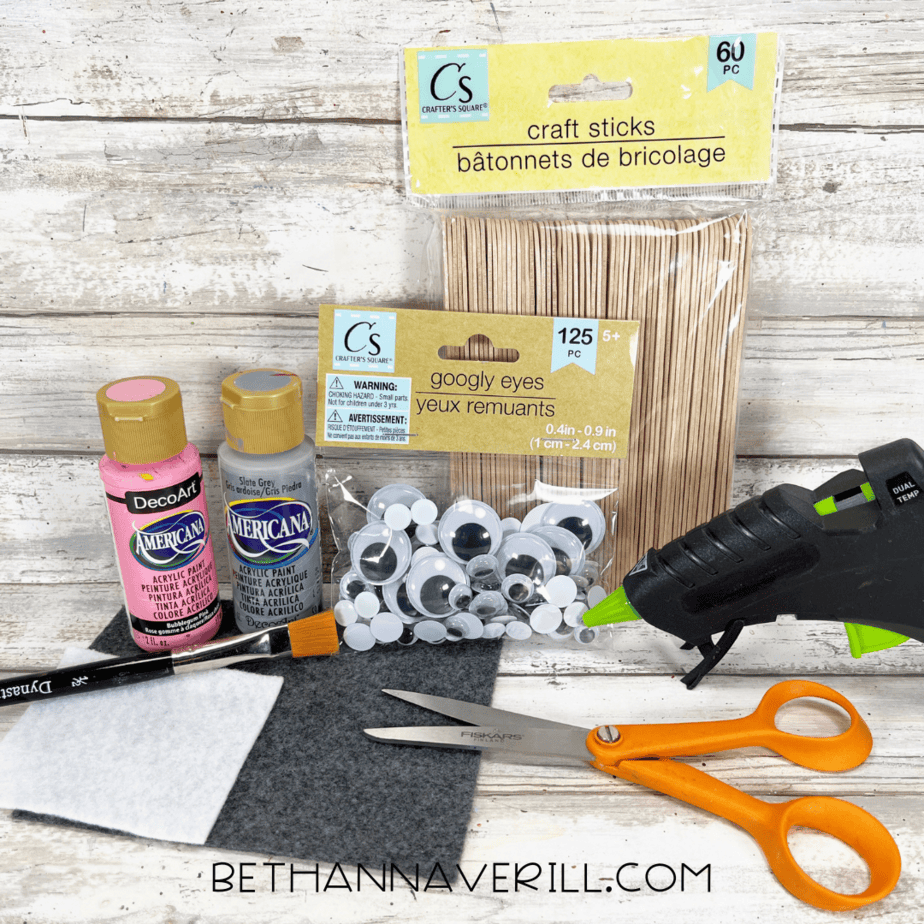 Craft supplies including paint, felt, googly eyes, glue, scissors, and craft sticks laid out on a table.