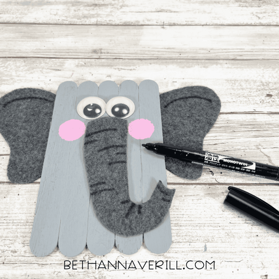 Black marker adding details to the elephant’s trunk and ears.