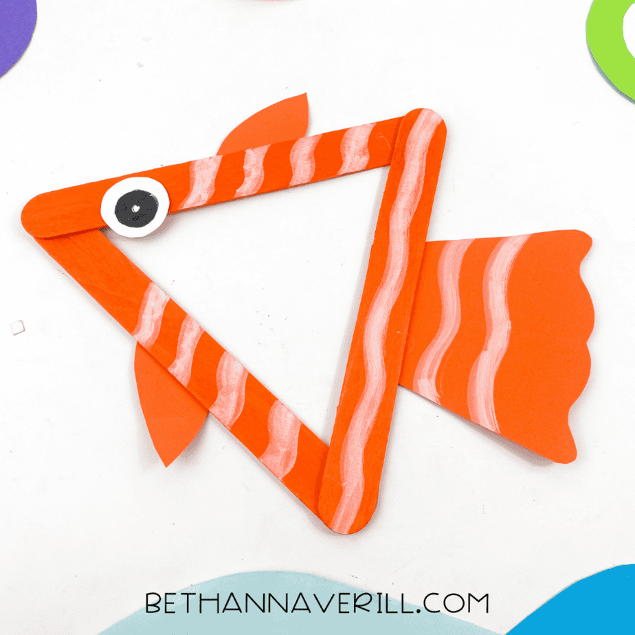 Finished fish popsicle stick craft displayed with ocean-themed background.