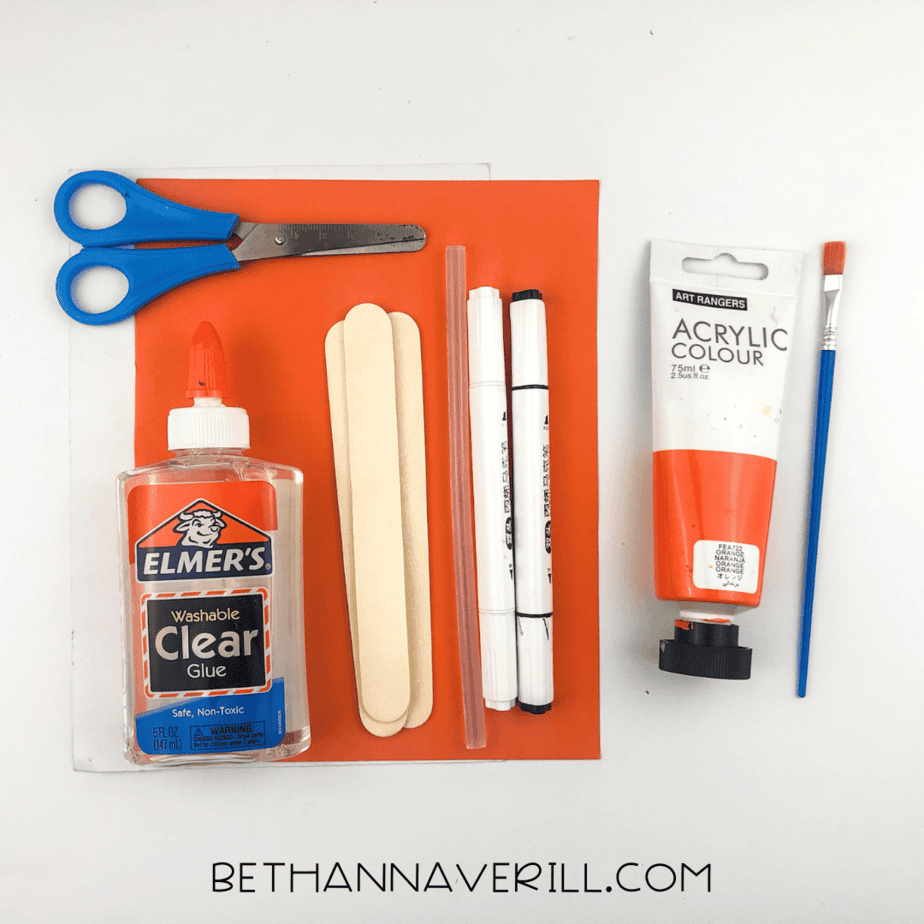 Materials for fish popsicle stick craft including orange paper, paint, glue, and scissors.