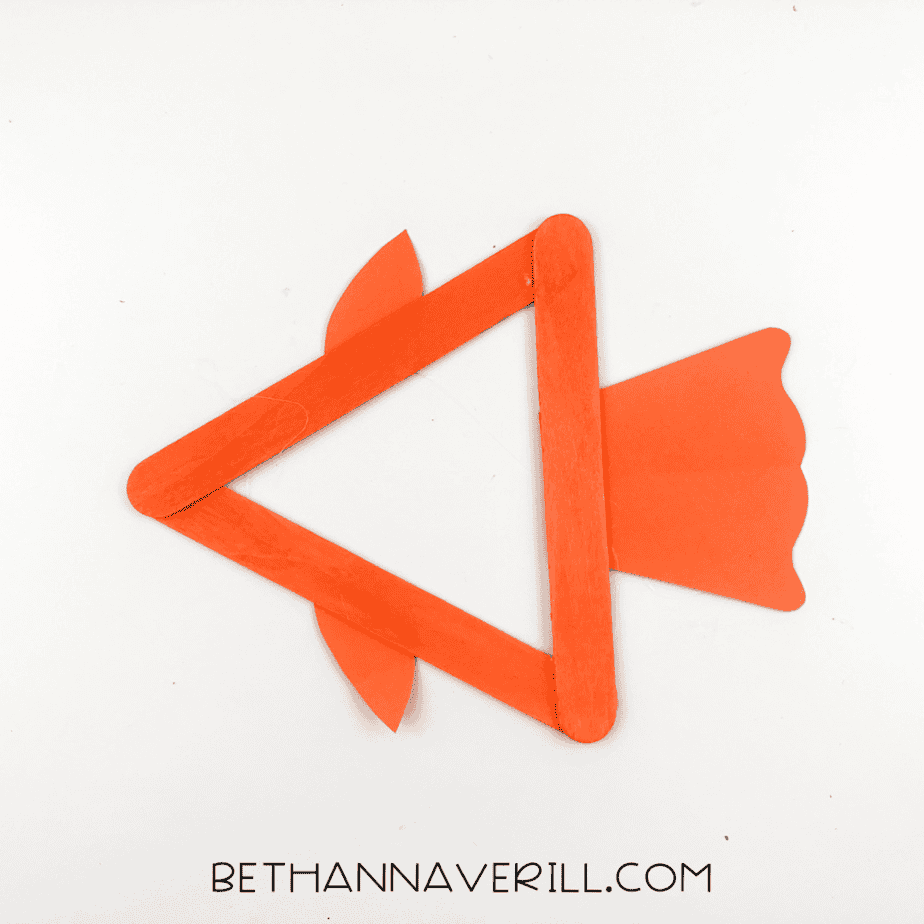 Triangle popsicle stick frame with orange fins and tail attached.