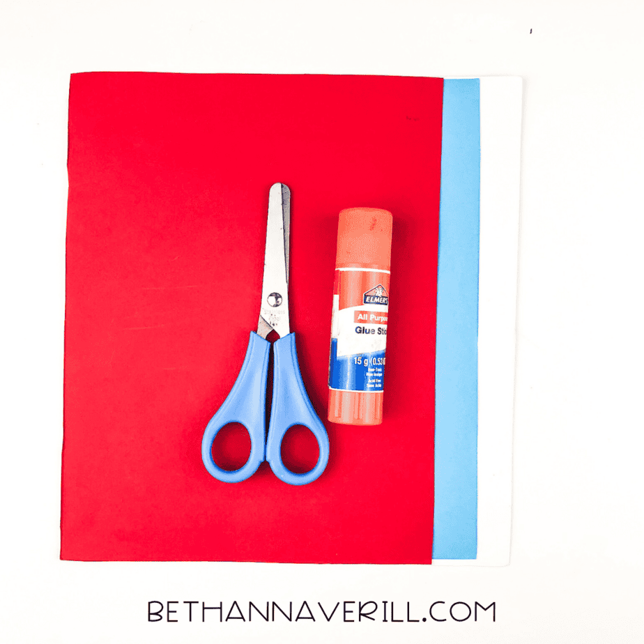 Craft materials including scissors, glue stick, and red, white, and blue construction paper
