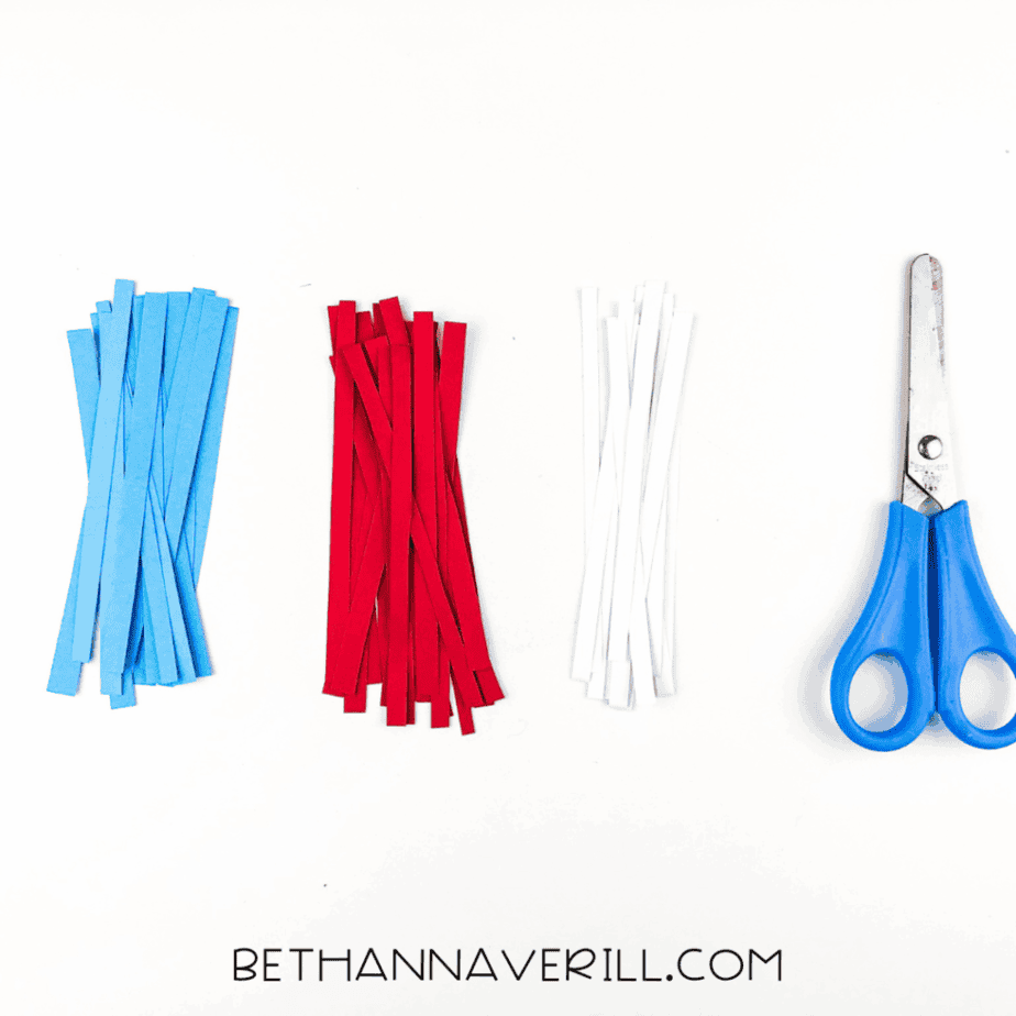 Strips of red, white, and blue paper lined up next to scissors