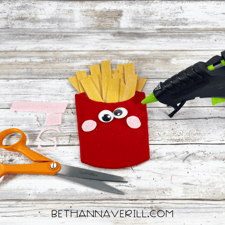 Red felt fry container with googly eyes and pink felt cheeks being glued on.
