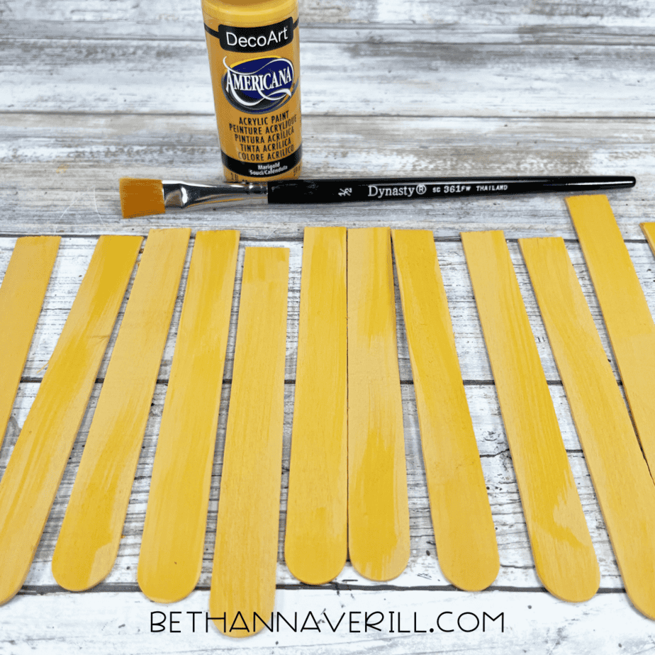Painted yellow craft sticks laid out to dry with paint bottle and brush.
