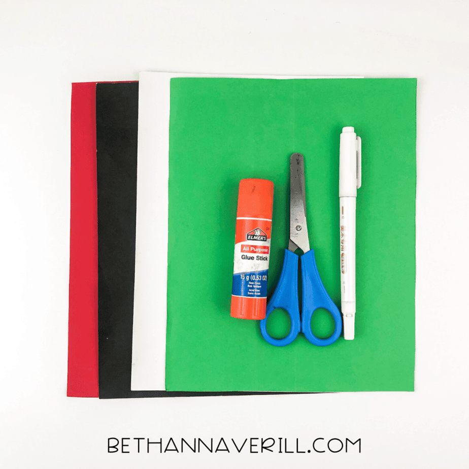 Materials for frog handprint craft: glue stick, scissors, black marker, and colored paper