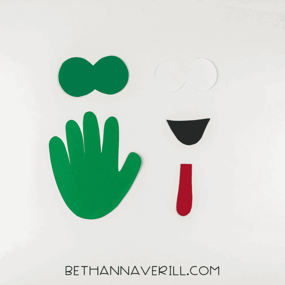 Materials for frog handprint craft: glue stick, scissors, black marker, and colored paper