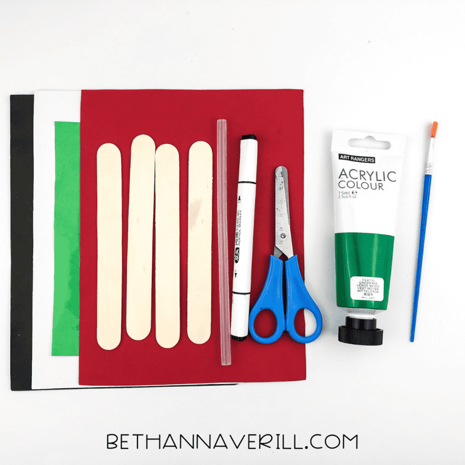 Craft supplies for frog popsicle stick craft including paint, scissors, glue, and colored paper.