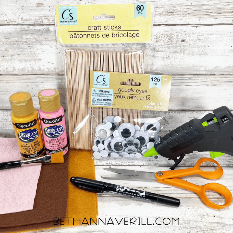 Craft materials for giraffe popsicle stick craft including felt, paint, googly eyes, glue gun, and scissors.