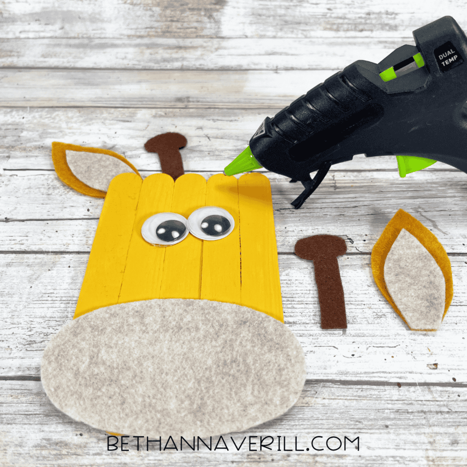 Yellow popsicle stick base with googly eyes, muzzle, and ear pieces ready to glue.