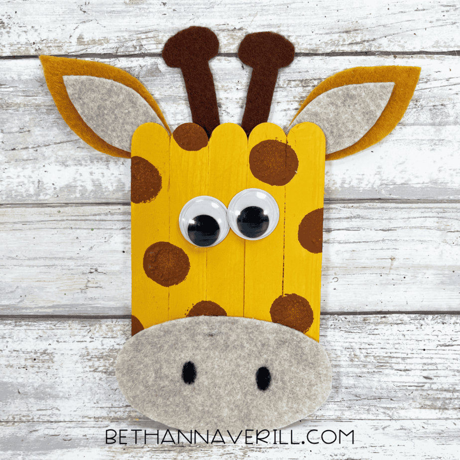 Finished giraffe popsicle stick craft with felt ears, muzzle, googly eyes, and painted details.
