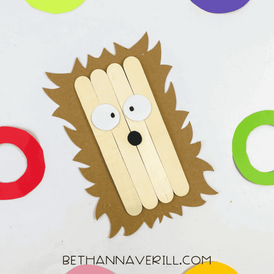 Finished hedgehog popsicle stick craft surrounded by colorful paper circles.
