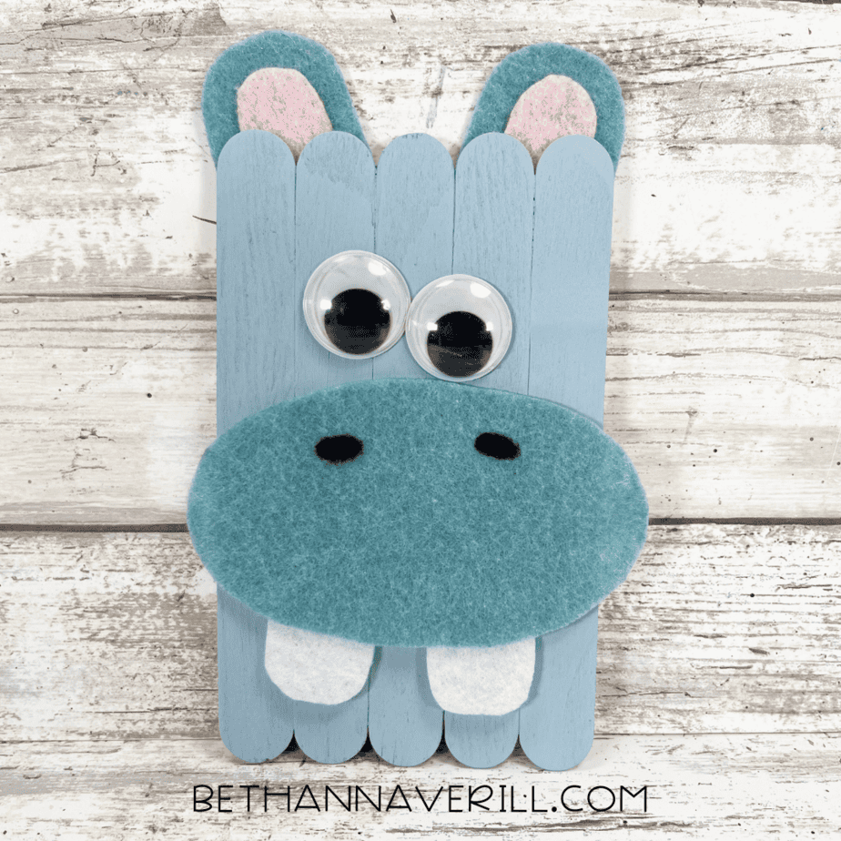 Completed hippo popsicle stick craft with blue paint, felt ears, googly eyes, and big white teeth.