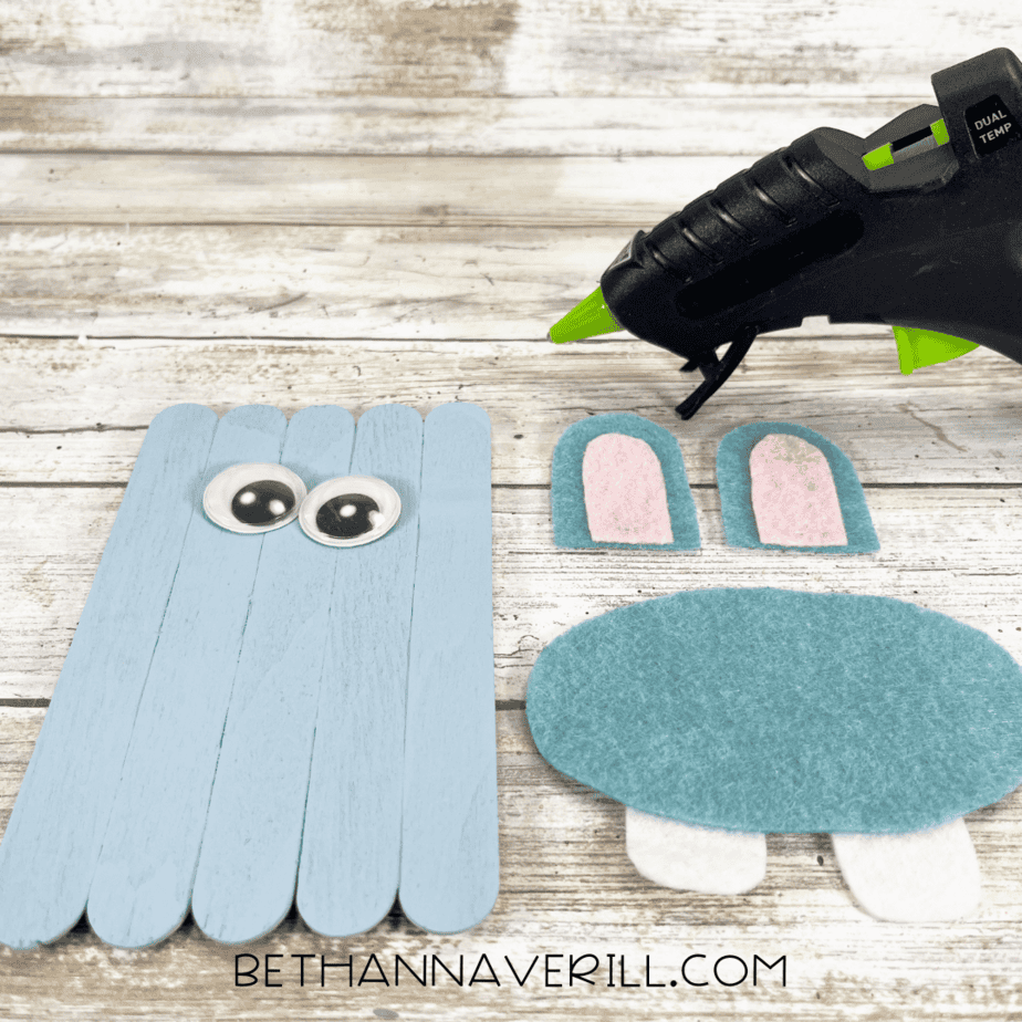 Painted popsicle stick base with googly eyes glued on, plus cut felt pieces ready to attach.