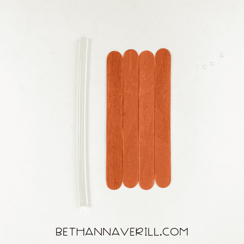 Brown-painted popsicle sticks lined up with a glue stick beside them.
