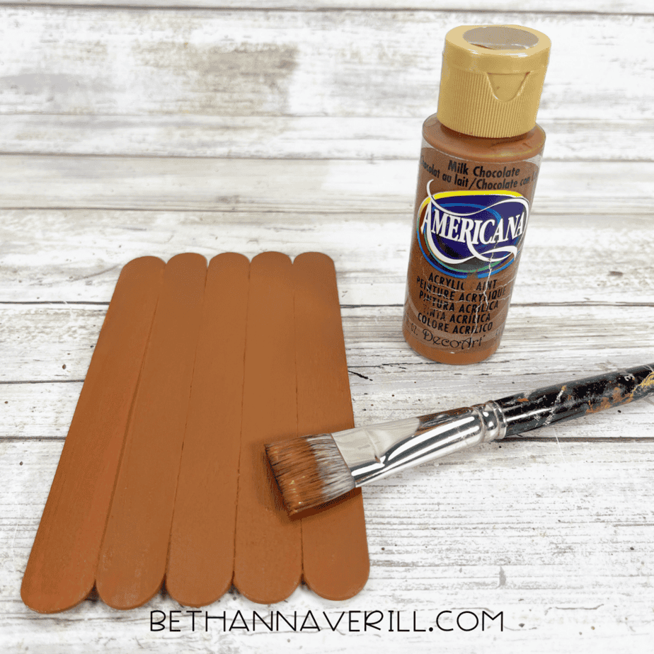 Craft sticks painted with brown acrylic paint and paintbrush resting on top.