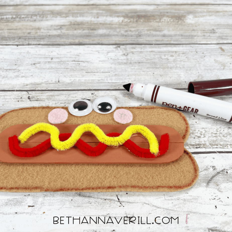 Brown marker adding final details to hot dog popsicle stick craft