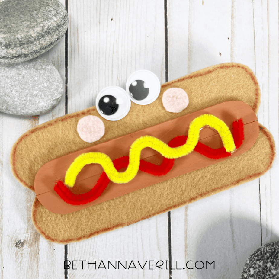 Completed hot dog popsicle stick craft with felt bun, googly eyes, and pipe cleaner toppings