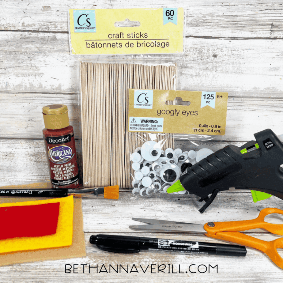 Craft supplies including felt, googly eyes, paint, pipe cleaners, glue gun, and scissors for hot dog popsicle stick craft