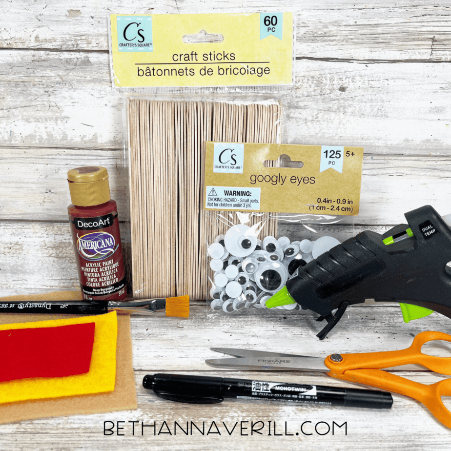 Craft supplies including felt, googly eyes, paint, pipe cleaners, glue gun, and scissors for hot dog popsicle stick craft