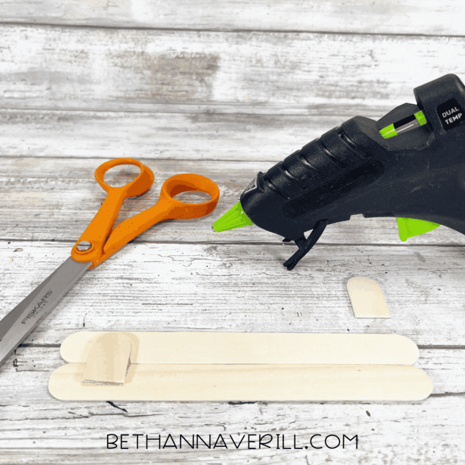 Two craft sticks being glued together with a glue gun