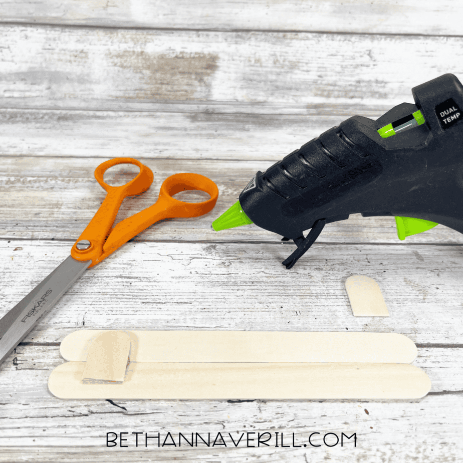 Two craft sticks being glued together with a glue gun