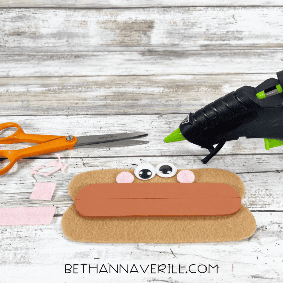 Googly eyes and pink felt cheeks glued to hot dog craft