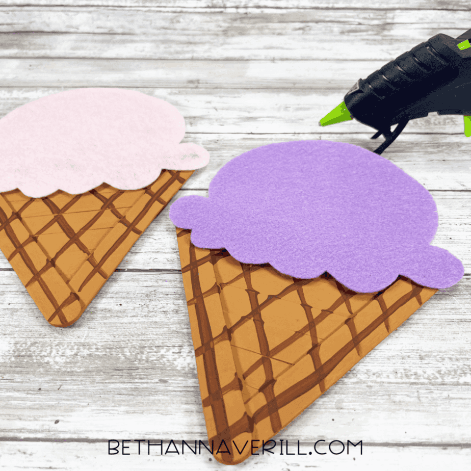 felt ice cream scoops glued to painted waffle cone bases made from popsicle sticks, with a glue gun nearby.
