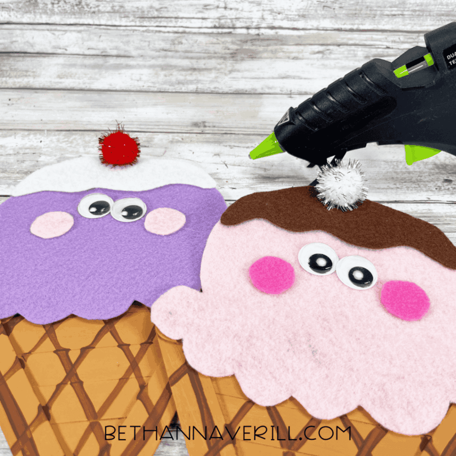 Hot glue gun adding pom-pom cherries to the top of the ice cream scoops.