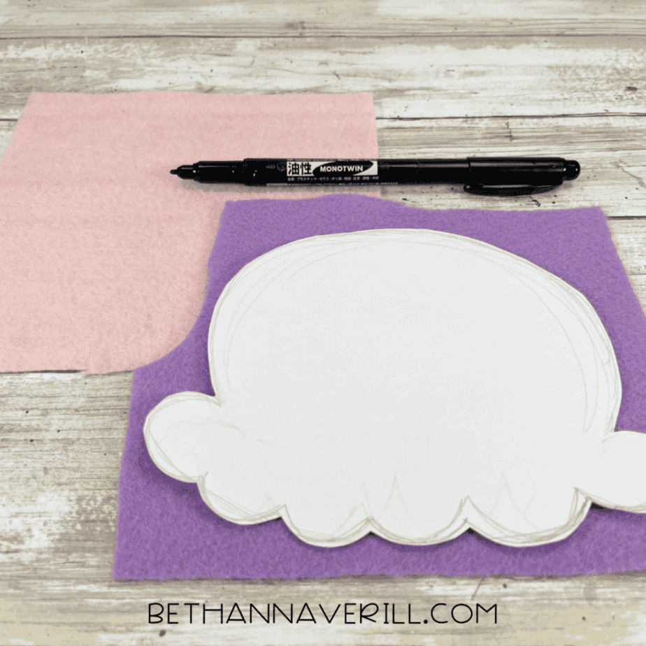 Pink and purple felt sheets with a paper ice cream scoop template placed on top, ready for tracing, along with a black marker.