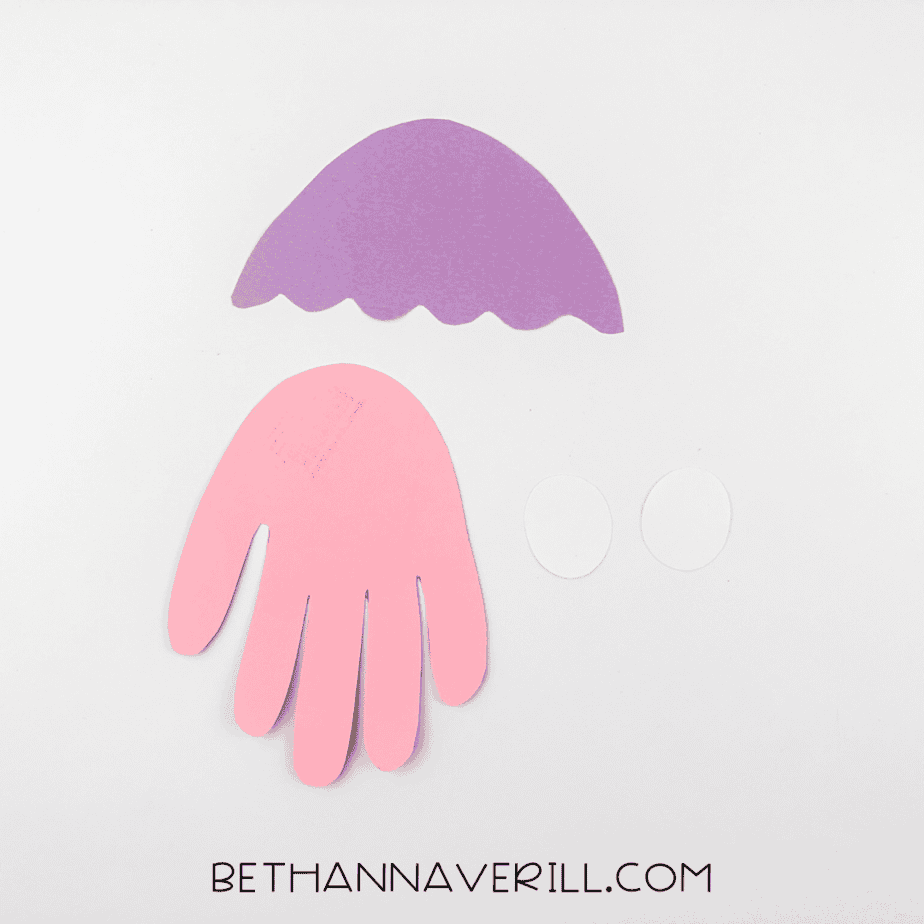 Cut-out pieces including pink handprint, purple dome, and white eye ovals