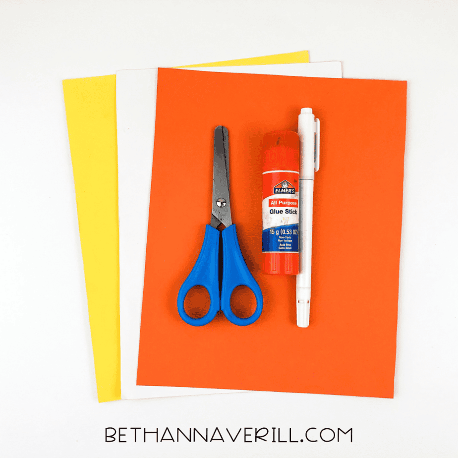 Craft supplies including orange, yellow, and white construction paper, glue stick, scissors, and black marker.