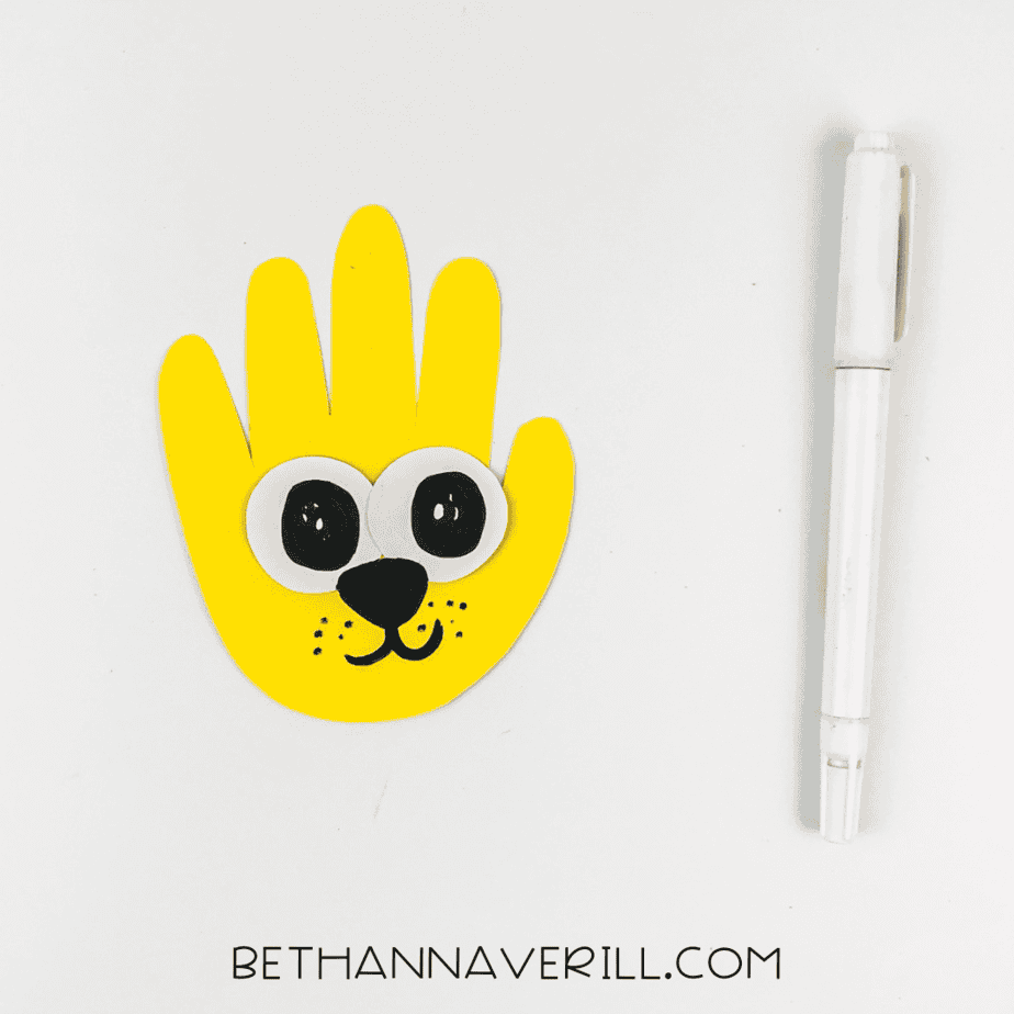 Finished lion face drawn on yellow handprint using black marker.